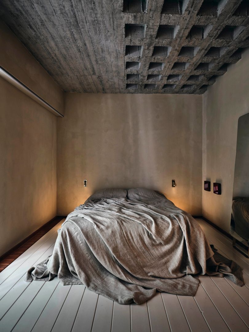 Minimalistisches Schlafzimmer mit Sichtbetondecke und Doppelbett in Erdtönen.