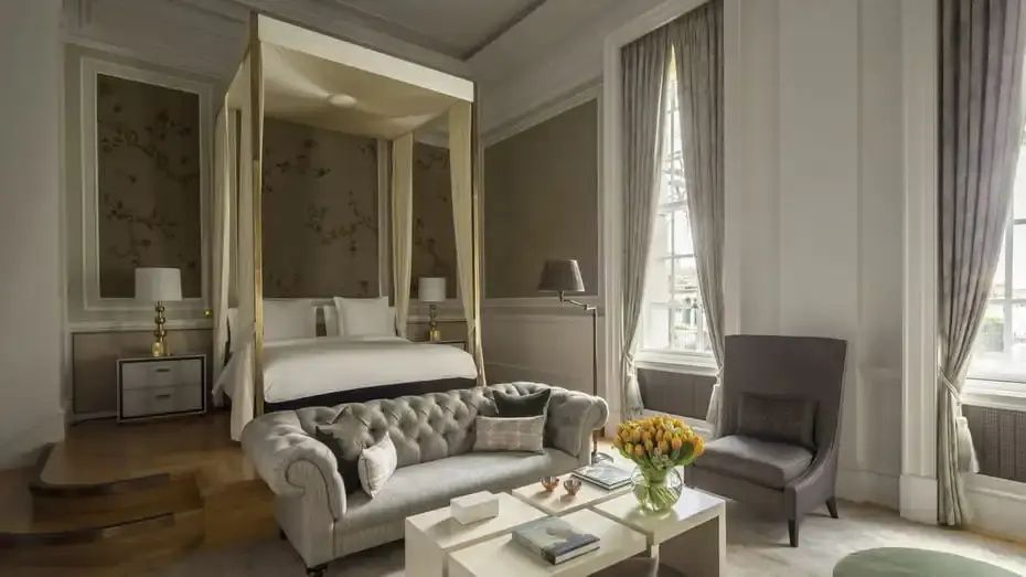 Großes Hotelzimmer mit einem Himmelbett, grauem Polstersofa und einem niedrigen Couchtisch.