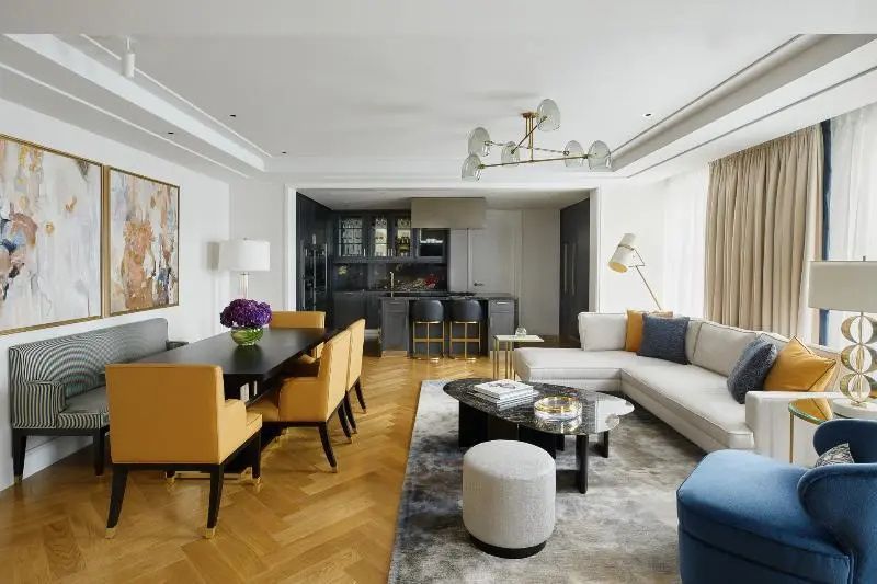 Wohnbereich einer Suite mit Esstisch, gelben Stühlen, Sofa und offener Küche im Hintergrund.