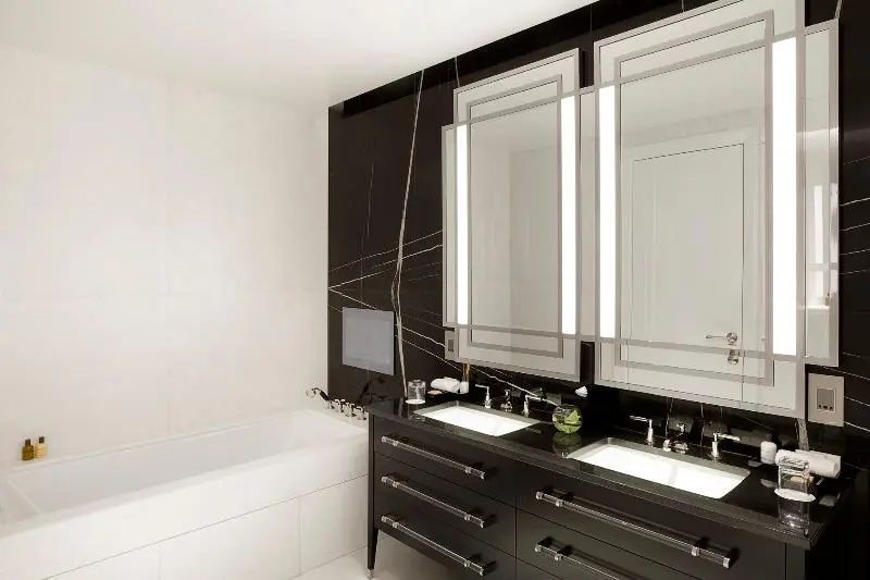 Badezimmer mit schwarzem Doppelwaschtisch, zwei beleuchteten Spiegeln und Badewanne.