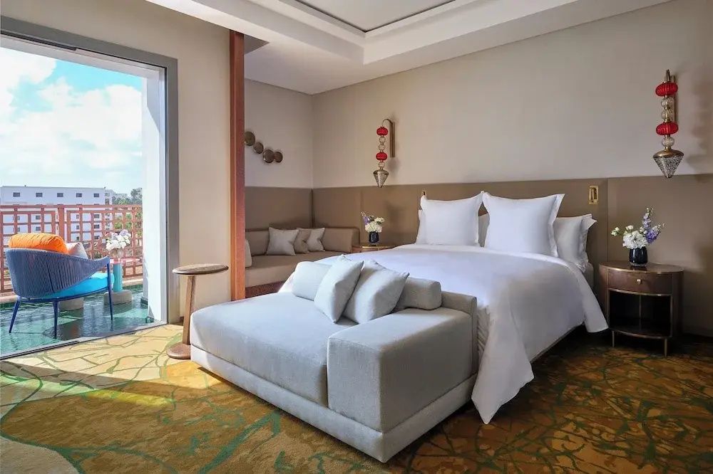 Hell eingerichtetes Hotelzimmer mit Doppelbett, Sitzbank und Balkonzugang.