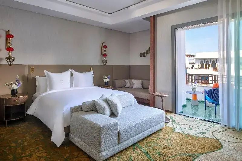 Hotelzimmer mit weißem Doppelbett, gepolsterter Sitzbank und offenem Balkon.