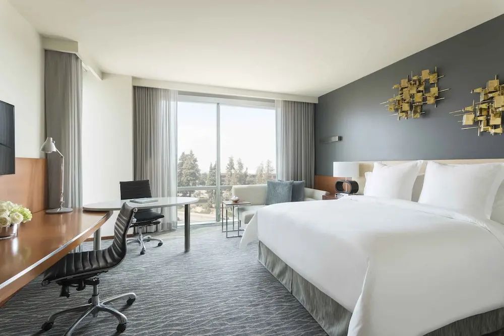 Helles Hotelzimmer mit großem Doppelbett, Schreibtisch und Fenster mit Blick nach draußen.