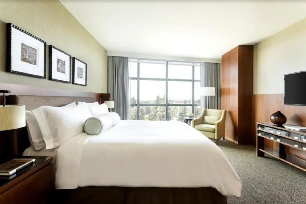 Helles Hotelzimmer mit großem Doppelbett, einem grünen Sessel und einer breiten Fensterfront.