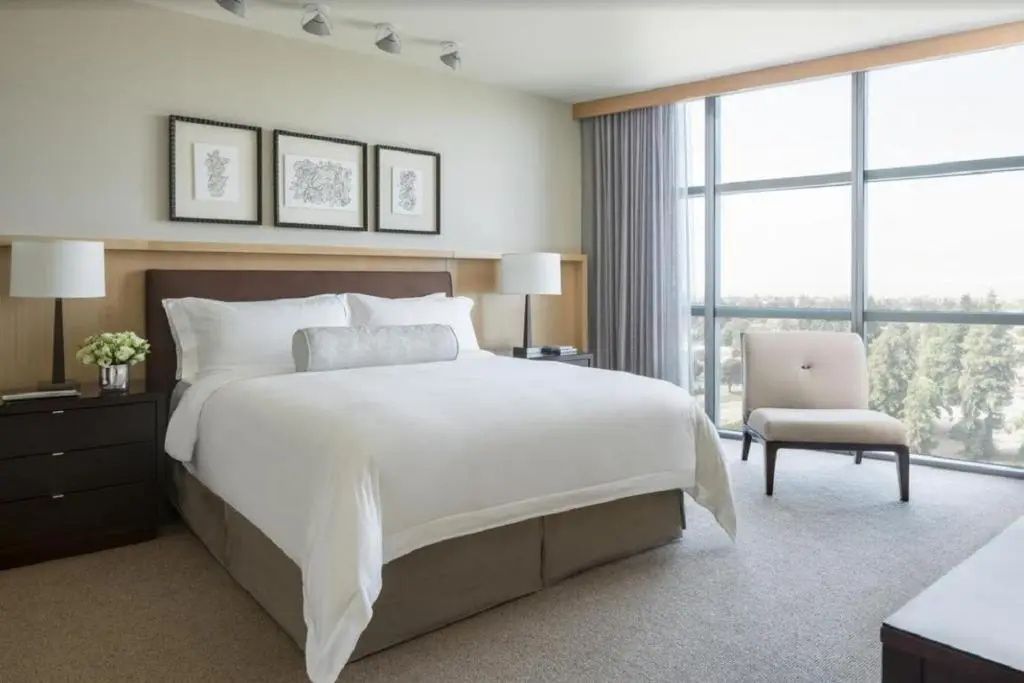 Helles Hotelzimmer mit großem Doppelbett, Sessel und bodentiefem Fenster.