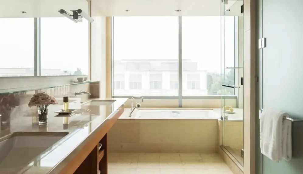 Badezimmer mit einer Badewanne am großen Fenster, Waschtisch und gläserner Dusche.