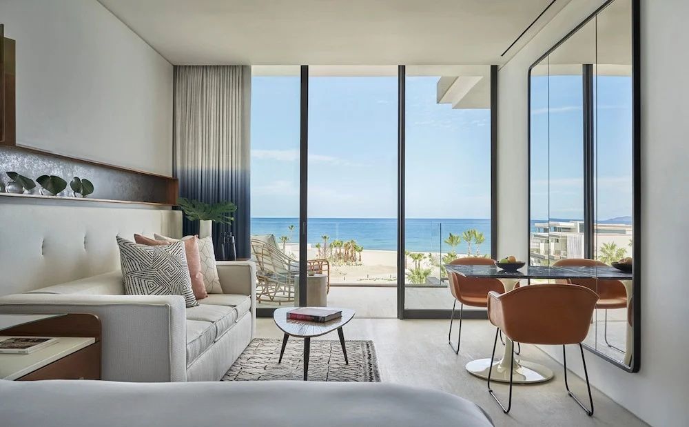 Wohnbereich eines Zimmers mit Panoramablick durch Glas-Schiebetüren auf Strand und Meer.