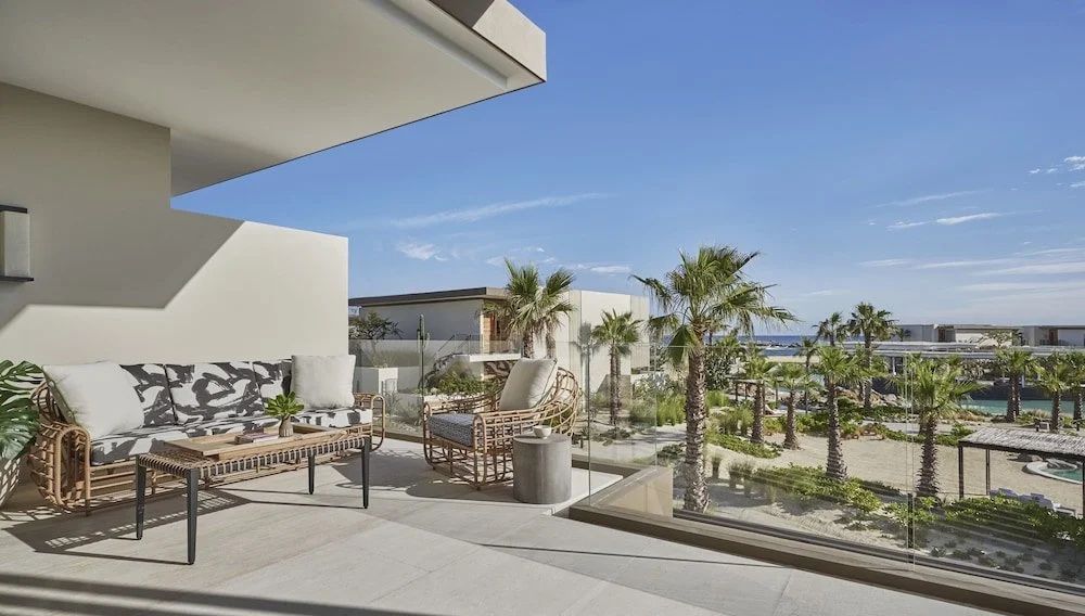 Terrasse mit Sitzmöbeln und Blick auf Palmen, den Strand und das Meer.