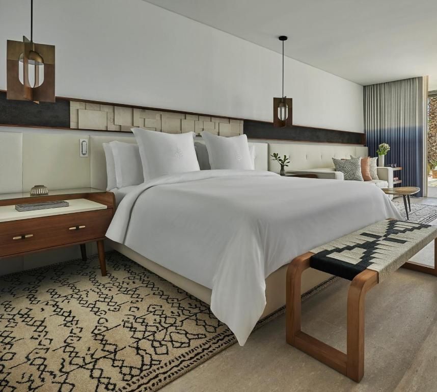 Hell eingerichtetes Hotelzimmer mit einem großen Doppelbett, Nachttisch und Sitzbereich.