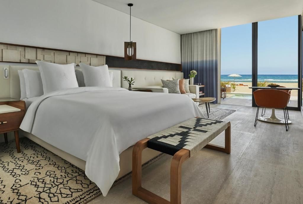 Helles Hotelzimmer mit Doppelbett, Sitzbank und Zugang zur Terrasse mit Meerblick