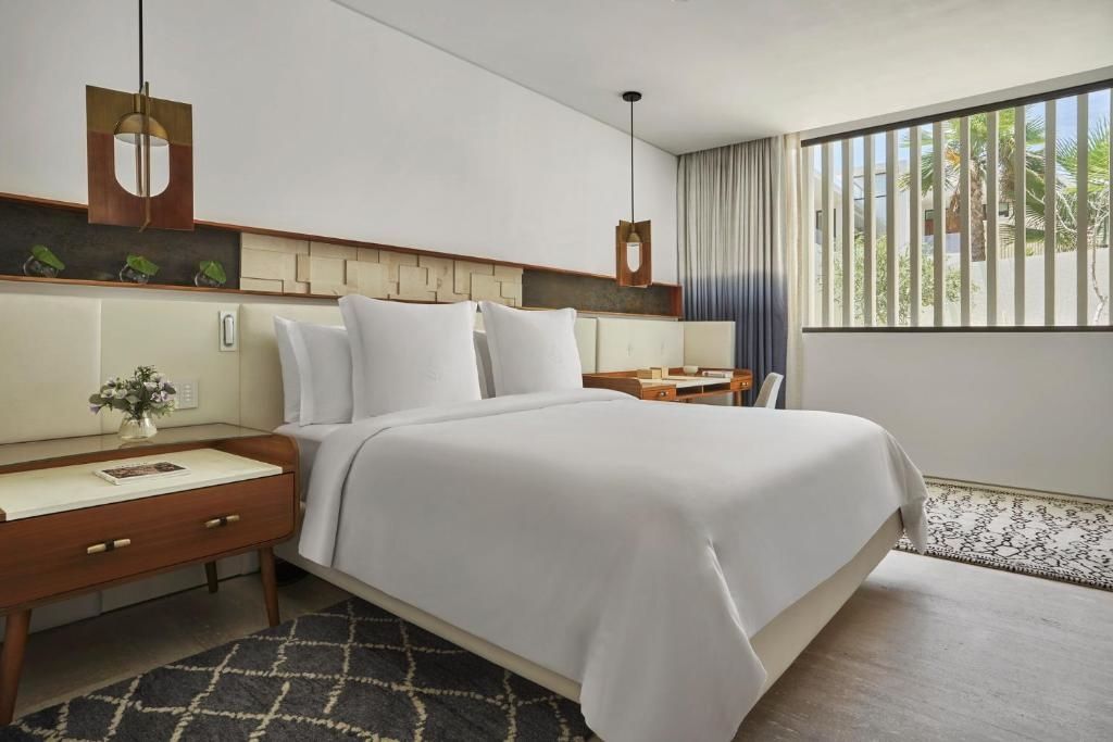 Schlafbereich eines Hotelzimmers mit großem Doppelbett, Schreibtisch und stilvoller Beleuchtung.