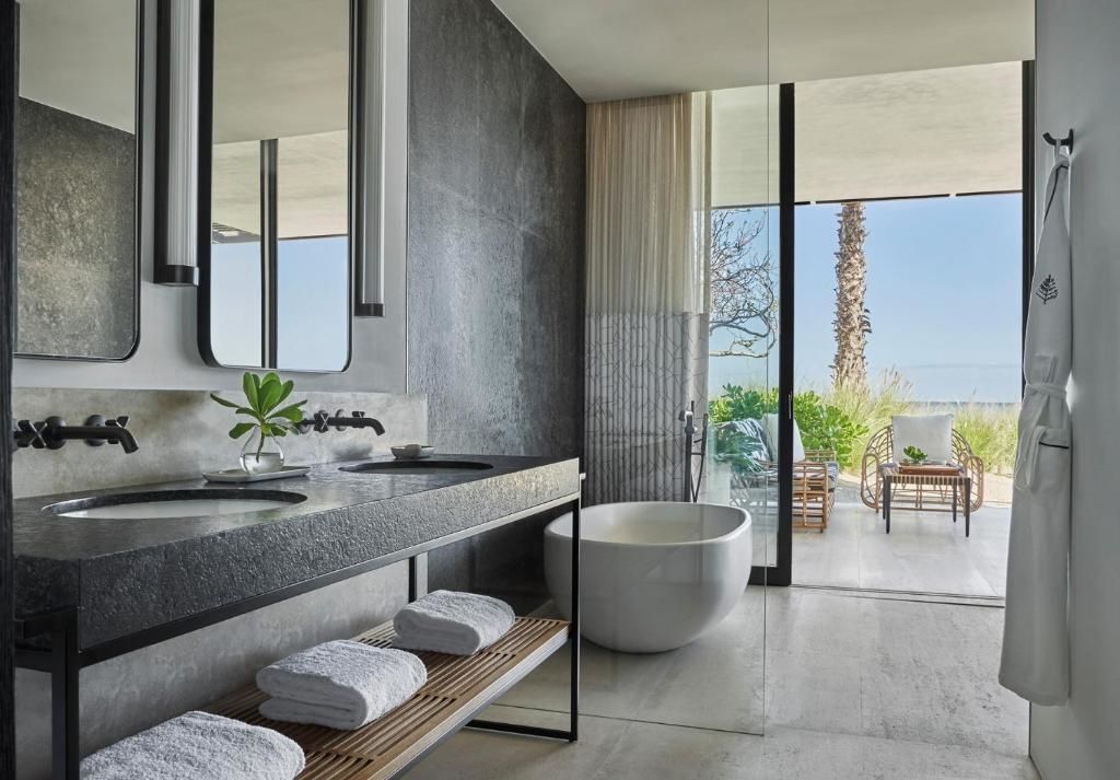 Badezimmer mit dunklem Doppelwaschtisch, freistehender Badewanne und Zugang zur Terrasse.