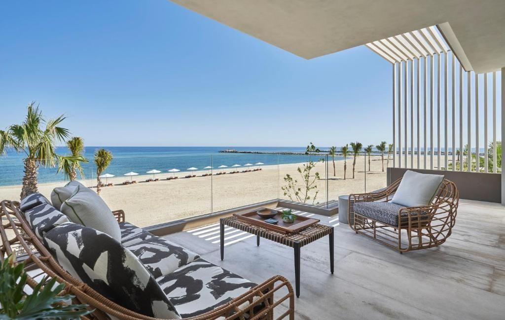 Terrasse mit Sitzmöbeln und freiem Blick auf den Sandstrand und das ruhige Meer unter blauem Himmel.