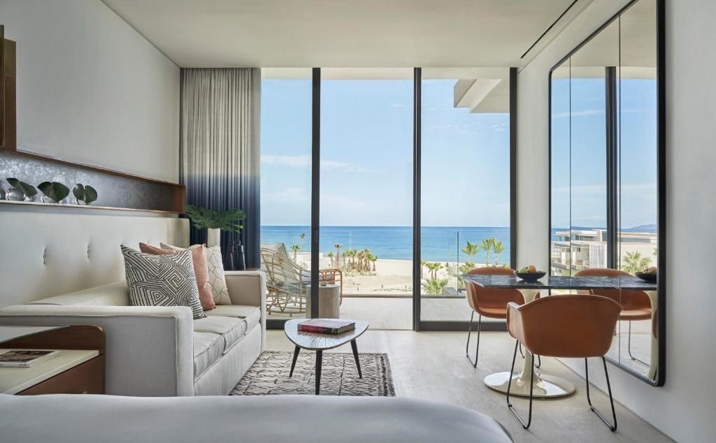 Wohnbereich im Hotelzimmer mit Sofa, Esstisch und bodentiefem Fenster zum Meer.