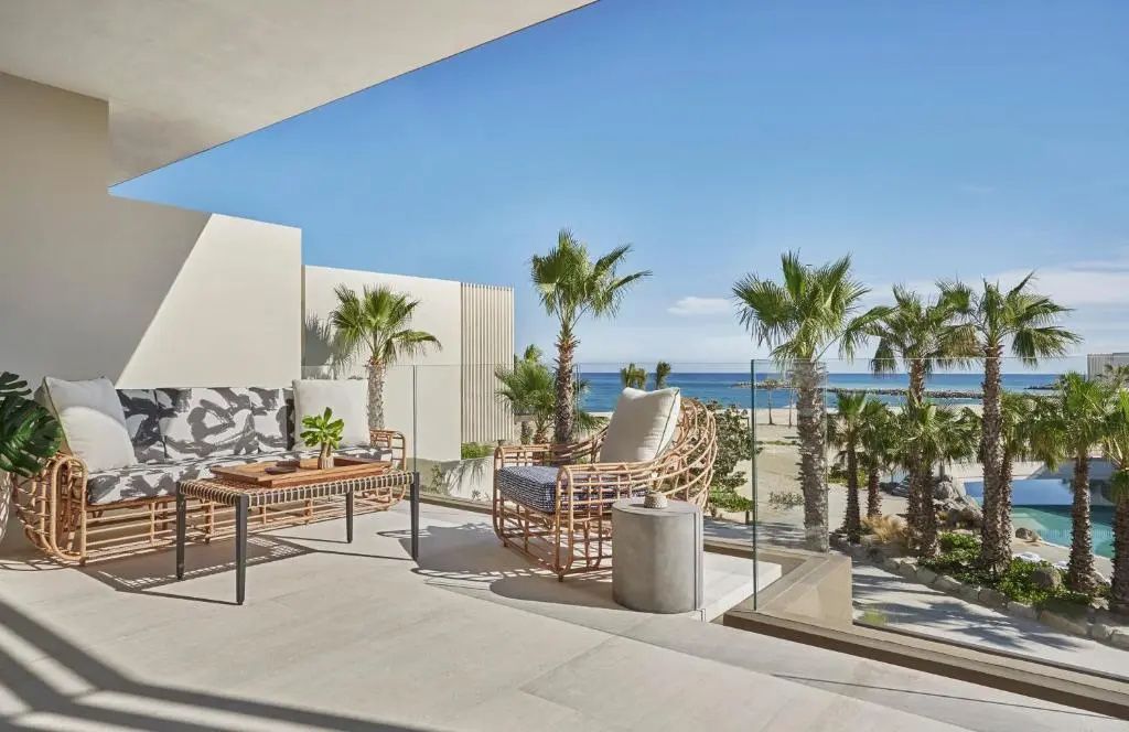 Terrasse mit Flechtsesseln, Couch und Glasgeländer mit Ausblick auf Palmen und das Meer.