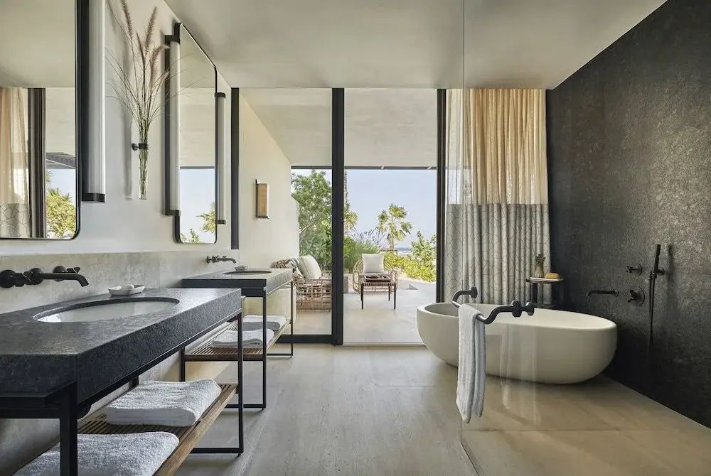 Badezimmer mit zwei Waschbecken, freistehender Badewanne und Zugang zur Terrasse.