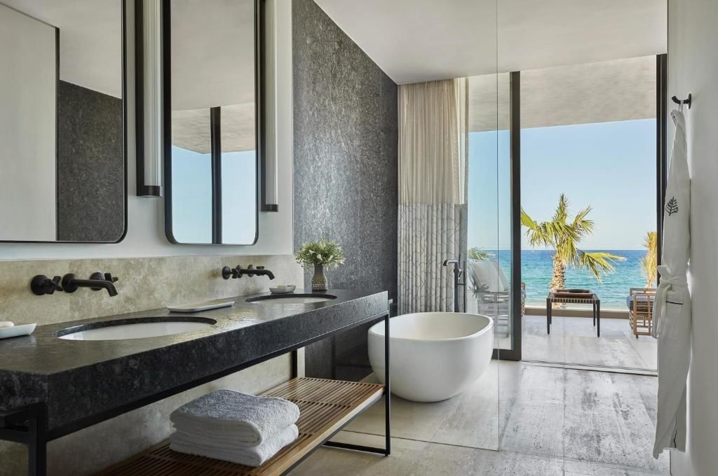 Badezimmer mit zwei Waschbecken, freistehender Wanne und verglastem Zugang zur Terrasse.