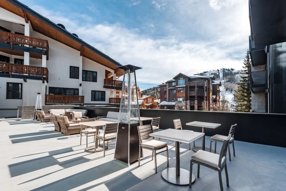 Terrasse mit Tischen, Stühlen und einem Heizstrahler vor verschneiter Bergkulisse.