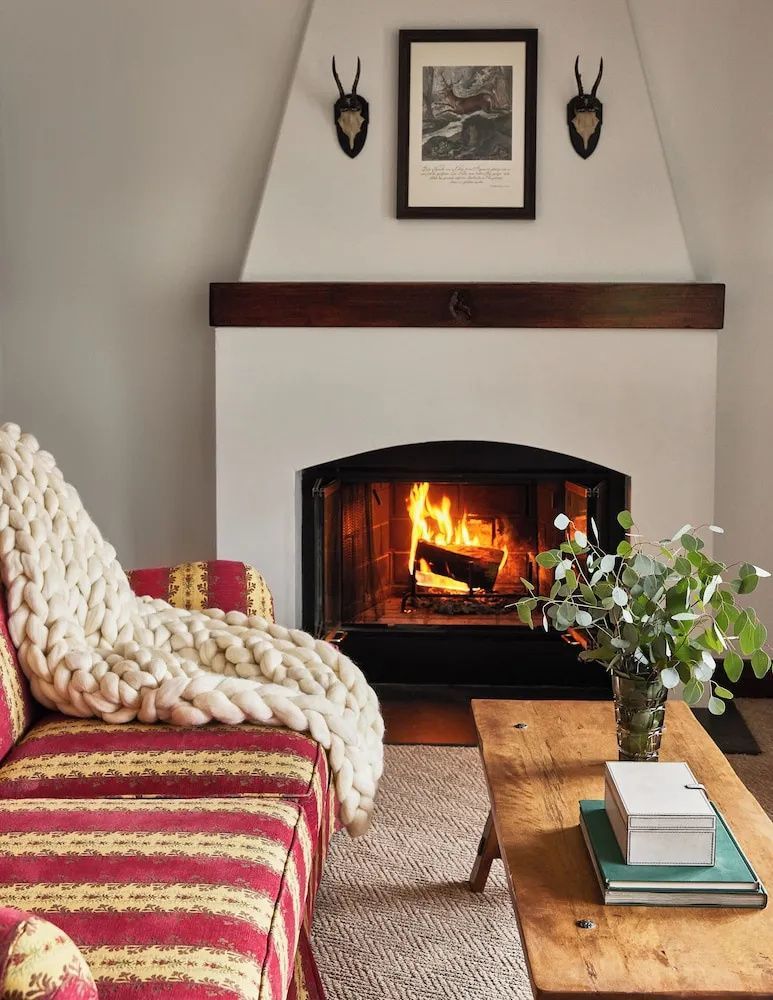 Brennender Kamin im Wohnbereich mit rot gemustertem Sofa und einem Holztisch.