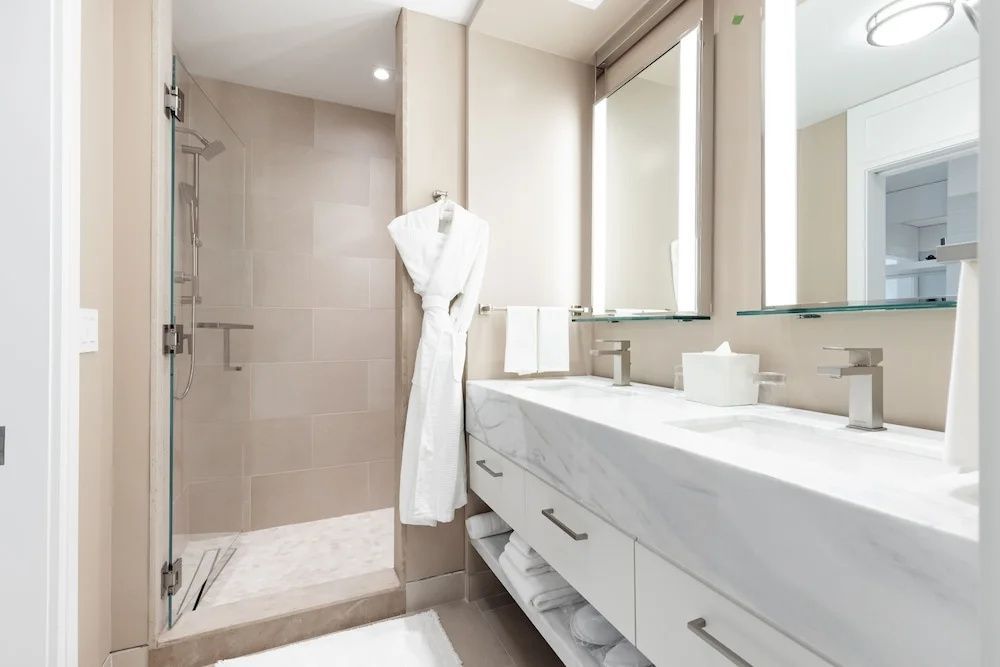 Helles Badezimmer mit langem Waschtisch, zwei beleuchteten Spiegeln und Dusche.