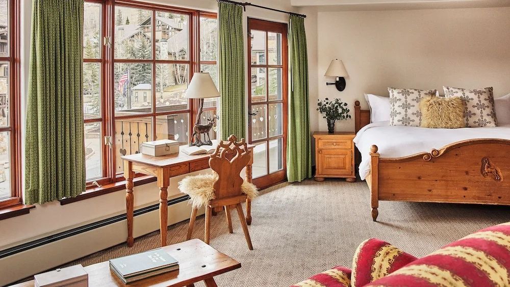 Hotelzimmer im alpenländischen Stil mit Holzschreibtisch, verziertem Stuhl und Fenster.