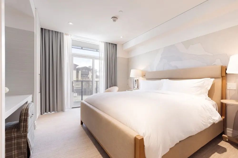 Modernes Schlafzimmer mit weiß eingedecktem Bett, hellem Teppich und Balkontür.