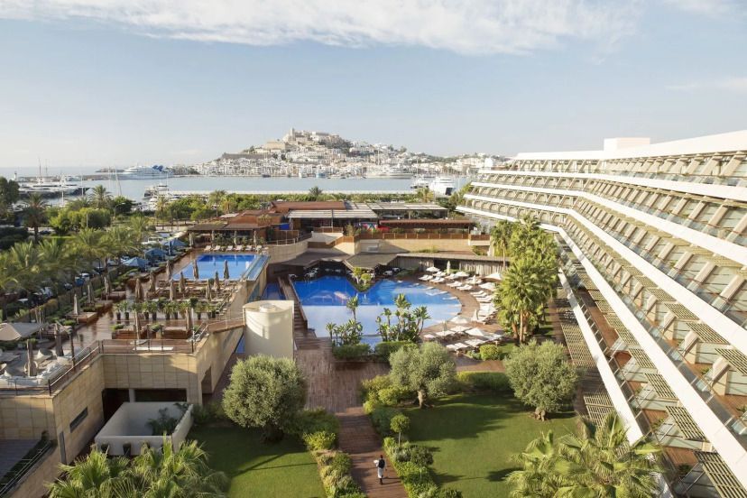 Luxuriöse Hotelanlage mit zwei Pools, viel Grünfläche und Blick auf die Altstadt von Ibiza und den Yachthafen.