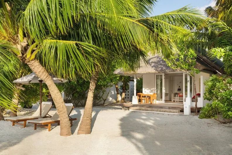 Strandbereich mit Palmen, Liegestühlen auf Sand und Holzterrasse der Villa