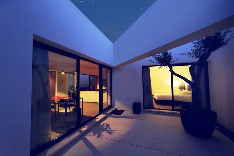 Beleuchteter Innenhof einer modernen Villa bei Nacht mit großzügigen Glasfronten.