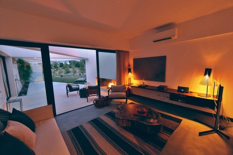 Wohnbereich einer Suite mit Sessel, Holztisch, Fernseher und Blick auf die beleuchtete Terrasse.