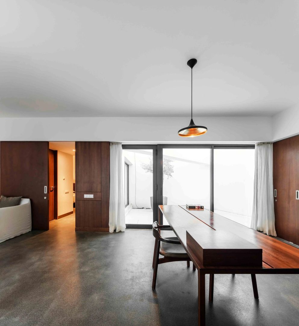 Moderner Wohnbereich mit langem Holztisch, dunklem Boden und großen Fensterfronten.