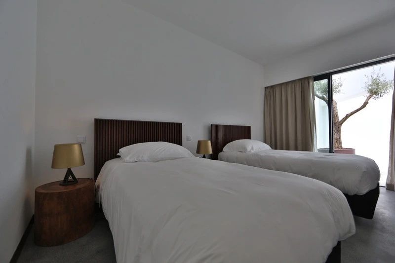 Schlafzimmer mit zwei Einzelbetten, braunen Kopfteilen und goldfarbenen Lampen auf den Nachttischen.