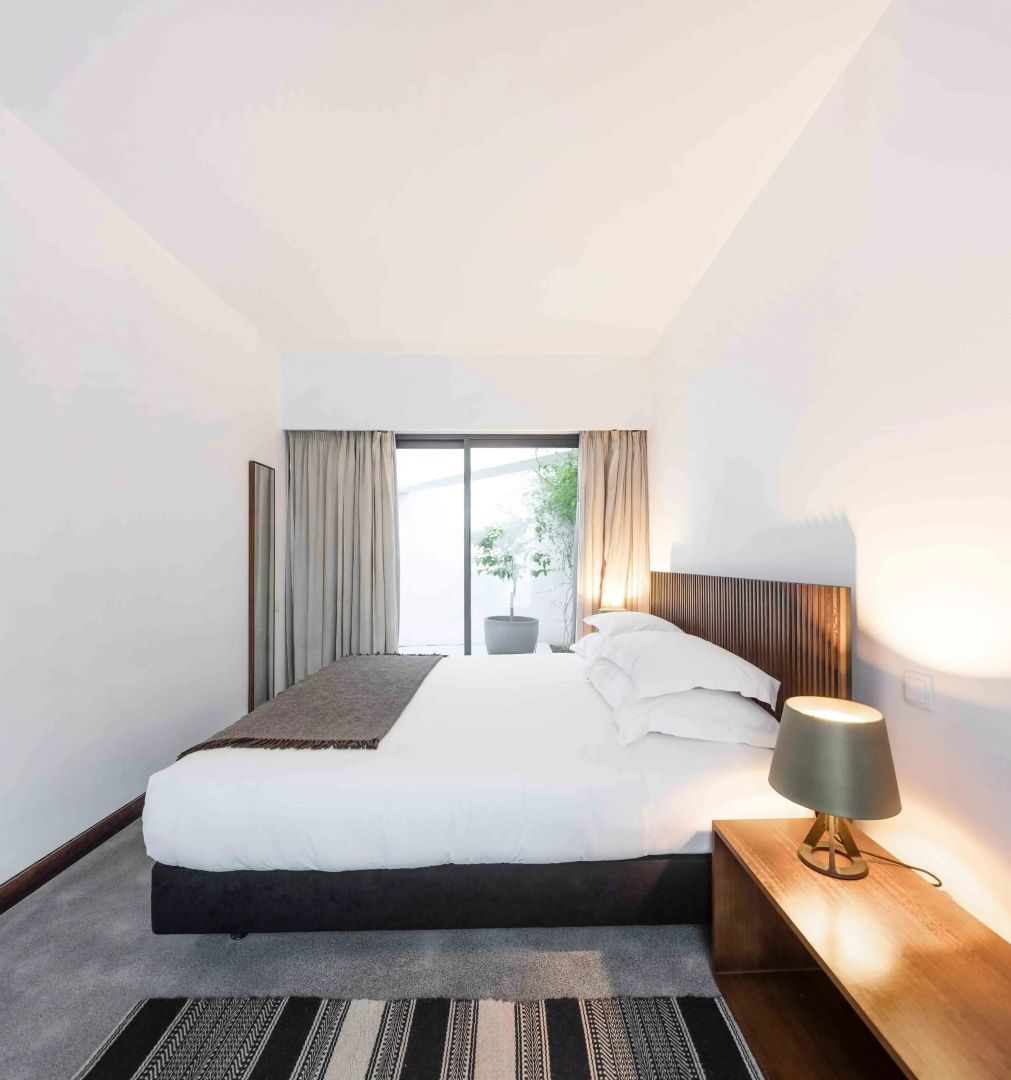 Hell eingerichtetes Schlafzimmer mit Doppelbett, Nachttisch und Blick auf die Terrasse.