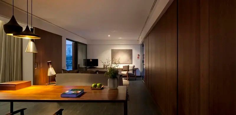 Wohnraum einer Suite mit Holztisch, Vasen Dekoration, Sofa und durchgehender Holzverkleidung.