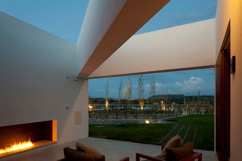 Blick von einer überdachten Terrasse auf ein Weinfeld und den Garten in der Abenddämmerung.