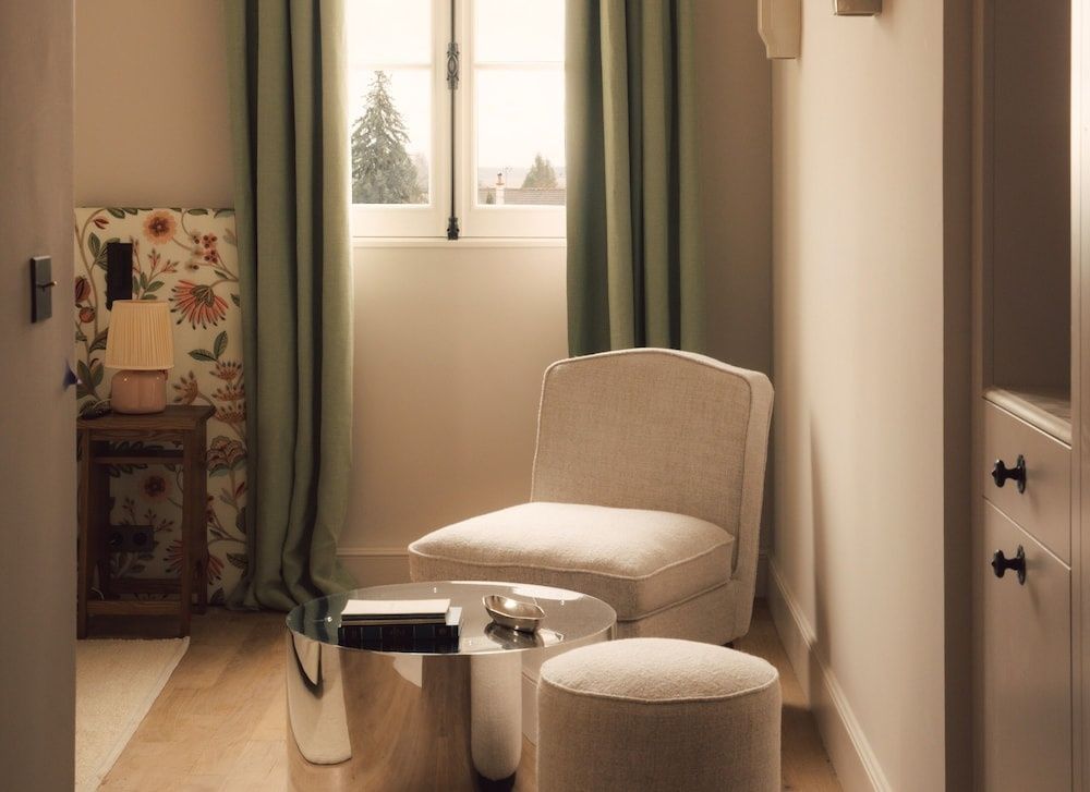 Sitzbereich im Hotelzimmer mit hellem Sessel, Beistelltisch und grünen Vorhängen.