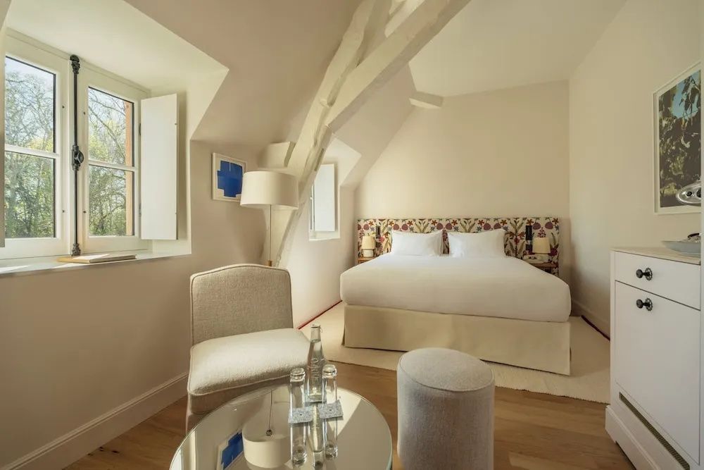 Helles Hotelzimmer unter der Dachschräge mit Doppelbett, Sessel und Couchtisch.