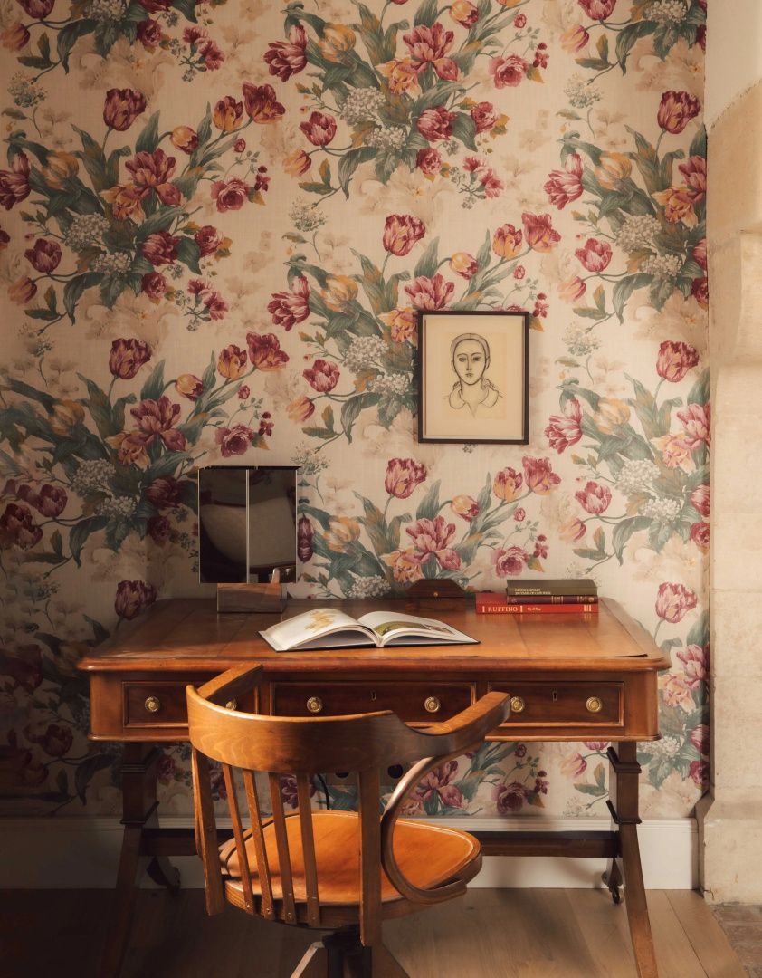 Holztisch mit Stuhl vor einer blumigen Tapete und einem kleinen gerahmten Bild an der Wand.