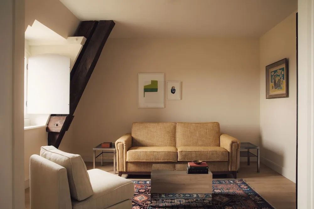 Sitzbereich in der Suite mit gelbem Sofa, Couchtisch, Teppich und Dachbalken.