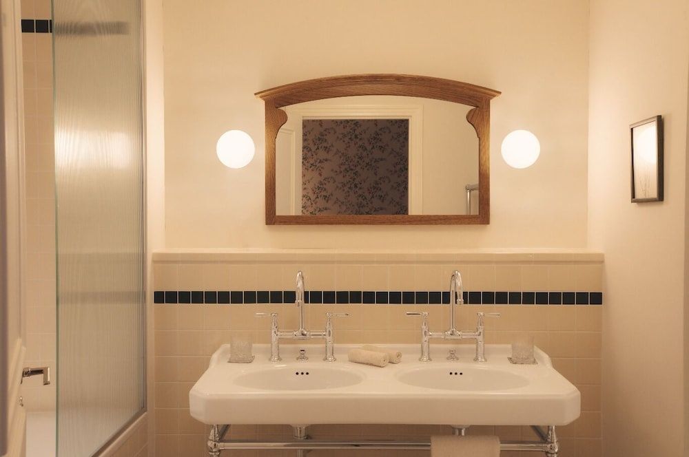 Doppelwaschbecken mit zwei Armaturen, großem Holzspiegel und Wandleuchten.