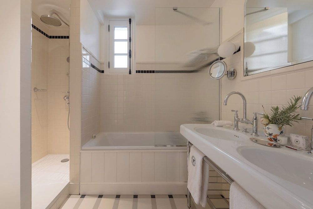 Hell gefliestes Badezimmer mit einer Badewanne, Duschkabine und zwei Waschtischen.
