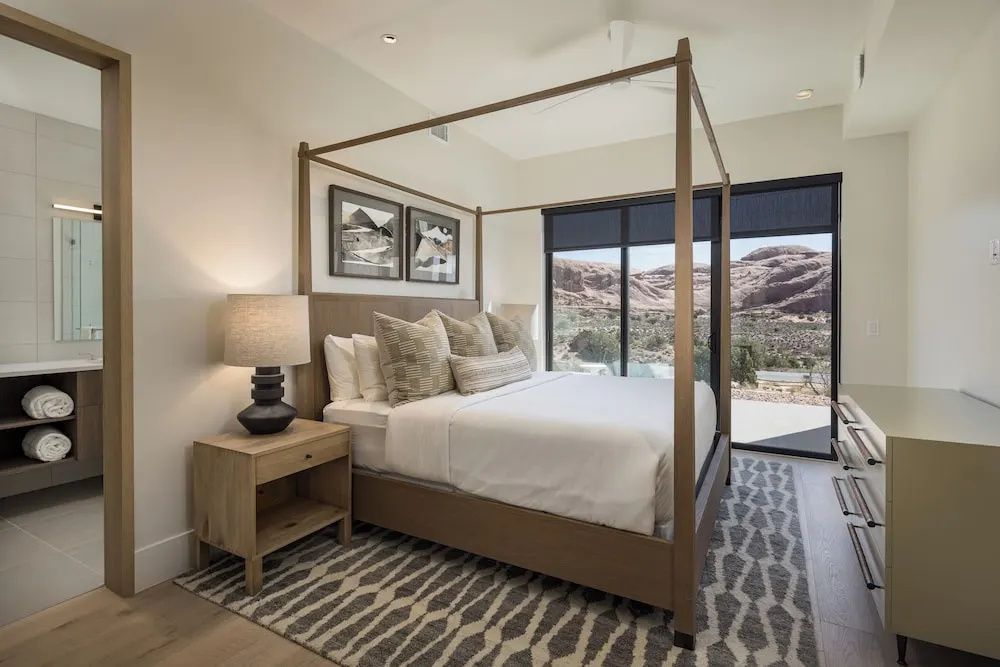 Schlafzimmer mit braunem Himmelbett, Nachttisch und Blick auf Felsen.