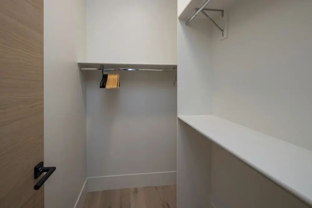 Begehbarer Kleiderschrank mit Holzboden, Kleiderstange und Wandregalen.