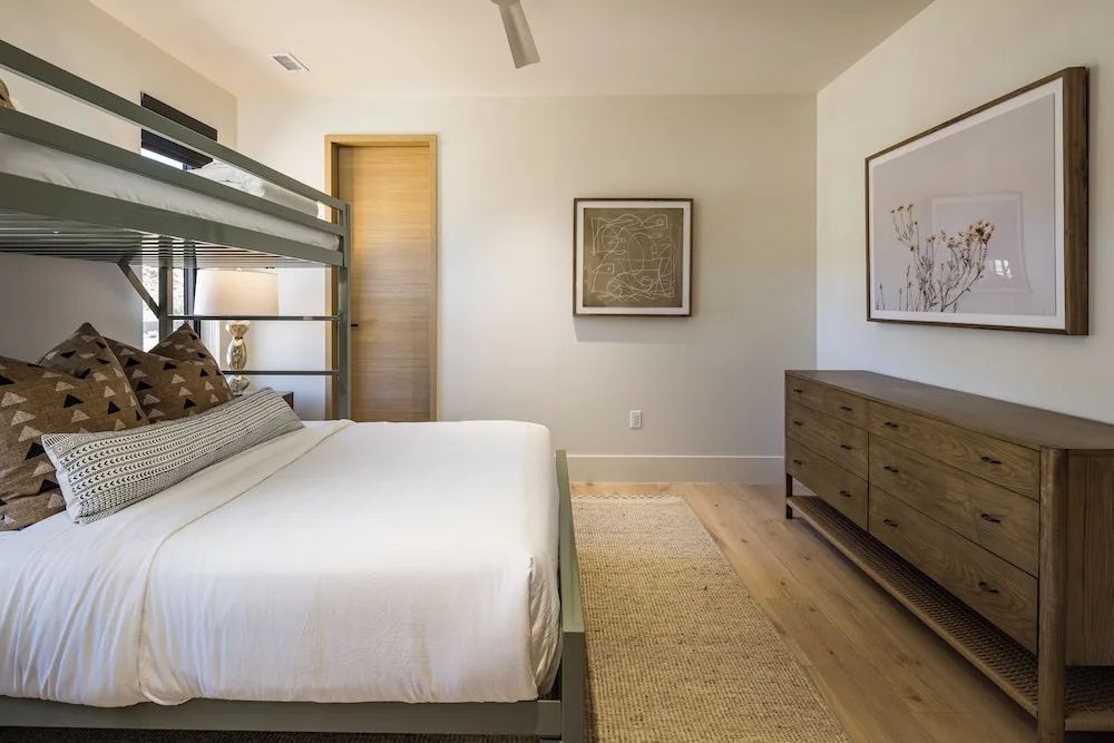 Schlafzimmer mit modernem Etagenbett, Holzkommode und hellem Teppich.