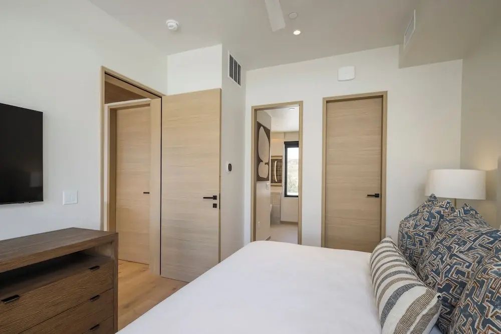 Helles Schlafzimmer mit Holztüren und weiß bezogenem Bett im Vordergrund.