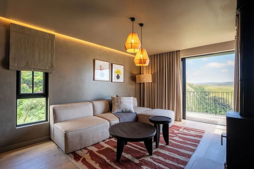 Sitzecke im Hotelzimmer mit beigefarbener Couch, Holz-Couchtischen und Wandbildern.