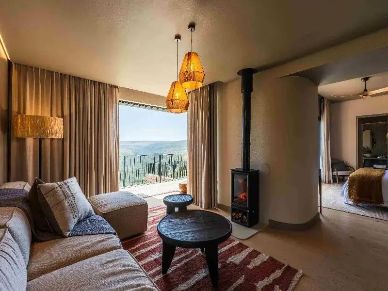 Wohnbereich einer Suite mit Sofa, zwei Holztischen, Kamin und Sicht ins Grüne.