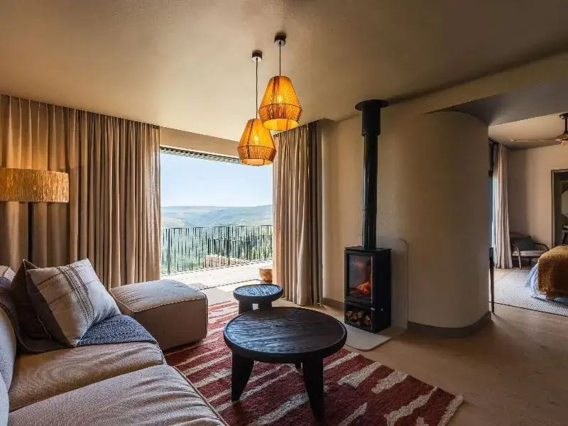 Sitzbereich im Hotelzimmer mit Kaminofen, Holz-Couchtischen und Panoramafenster.