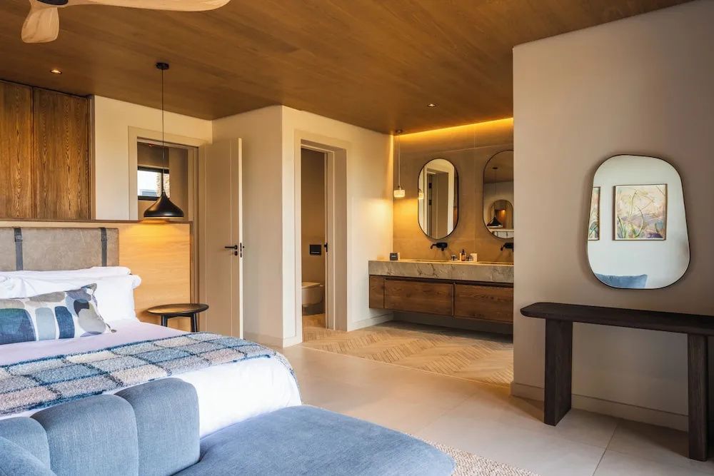 Modernes Hotelzimmer mit Bett, Holzdecke und offenem Waschbereich samt Doppelwaschbecken.