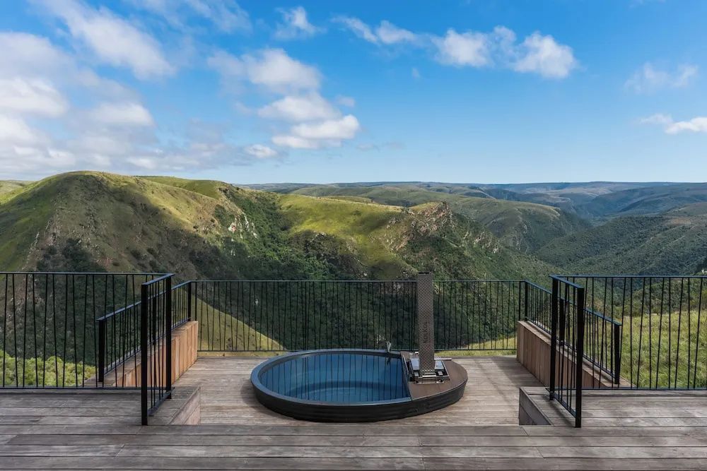 Runder Pool auf einer Holzplattform mit freiem Blick auf grüne Berge und ein Tal.